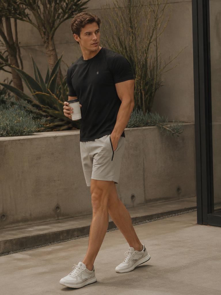 Model walking past a planted courtyard in a black tee and stone hybrid sport shorts