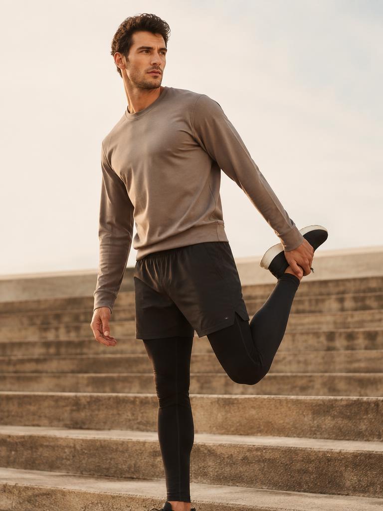 Man stretching on stone steps in taupe crew and black tights