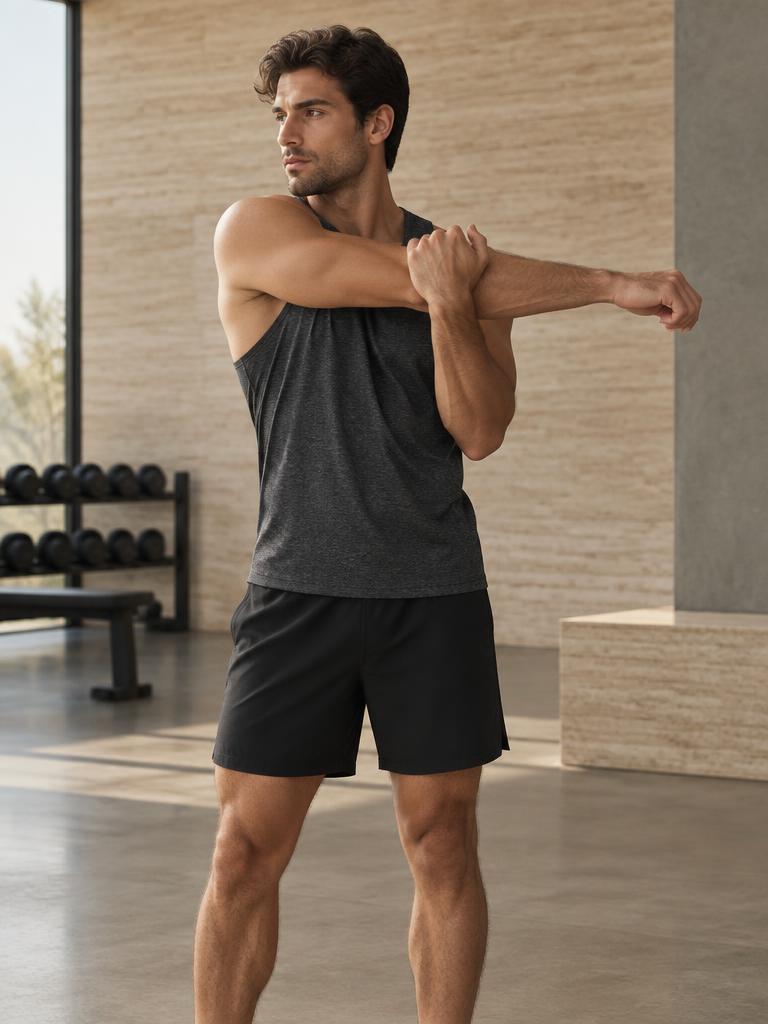 Man stretching in a charcoal training tank and black training shorts in a modern gym